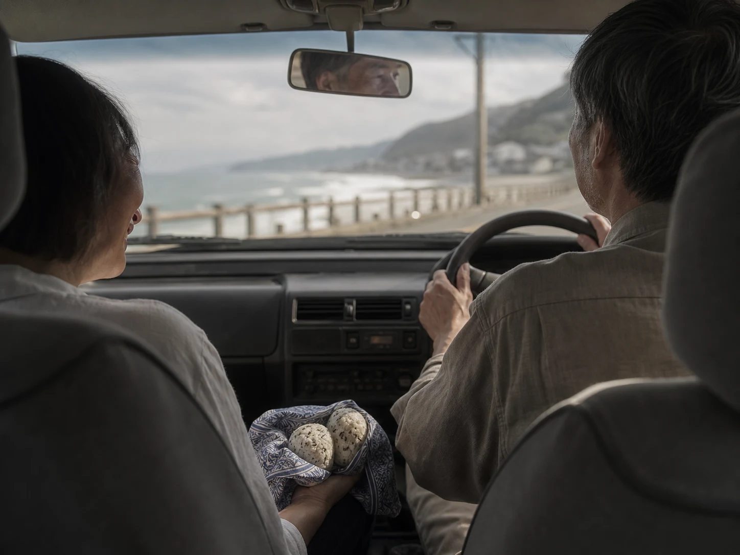 海沿いを走る車内。父の横顔がミラーに映り、母の手元におにぎりがある